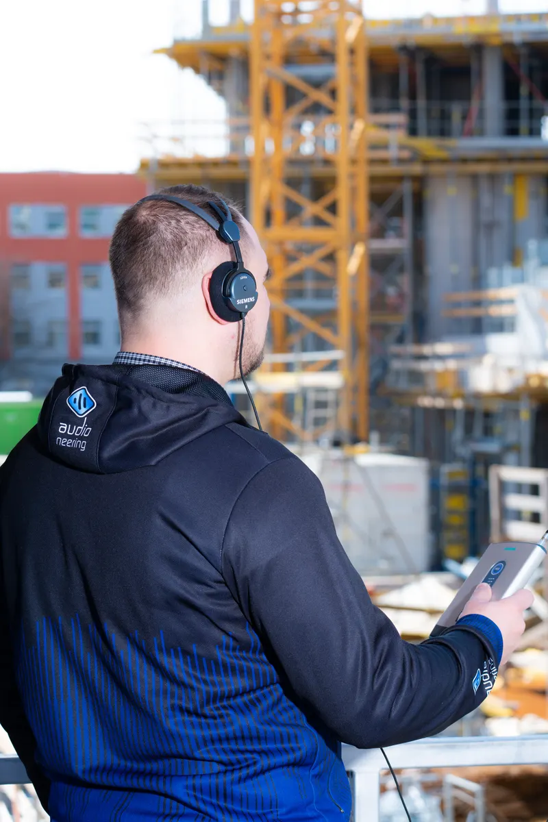 Roman Sereinig with headphones and a measuring device during a measurement on a building site.